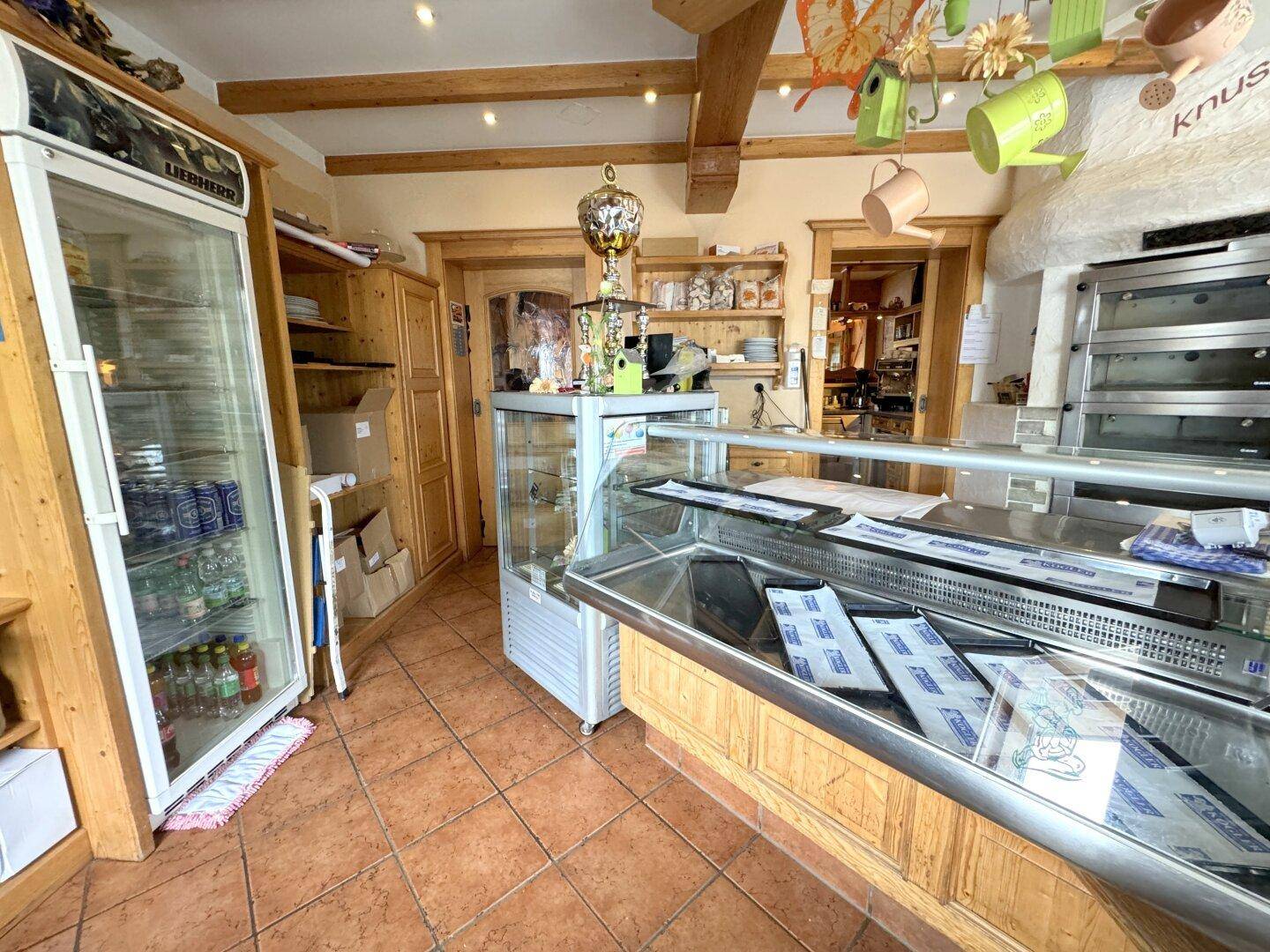 Verkaufsraum der Bäckerei mit Kühlvitrine, Regalen und Deckenbalken, die eine warme Atmosphäre schaffen.