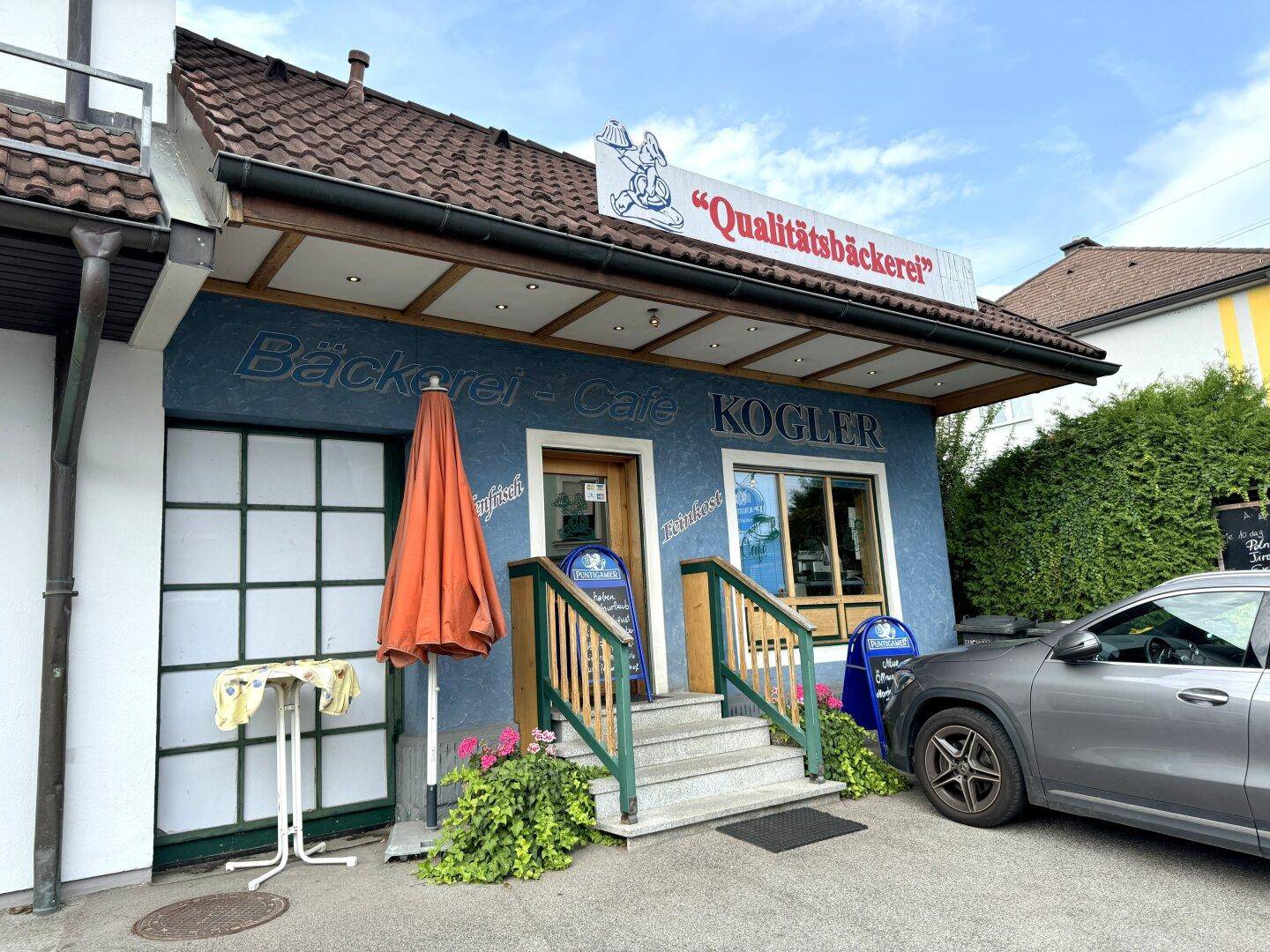 Nahaufnahme der Bäckerei-Café-Fassade mit Eingangsbereich und Werbeschildern.