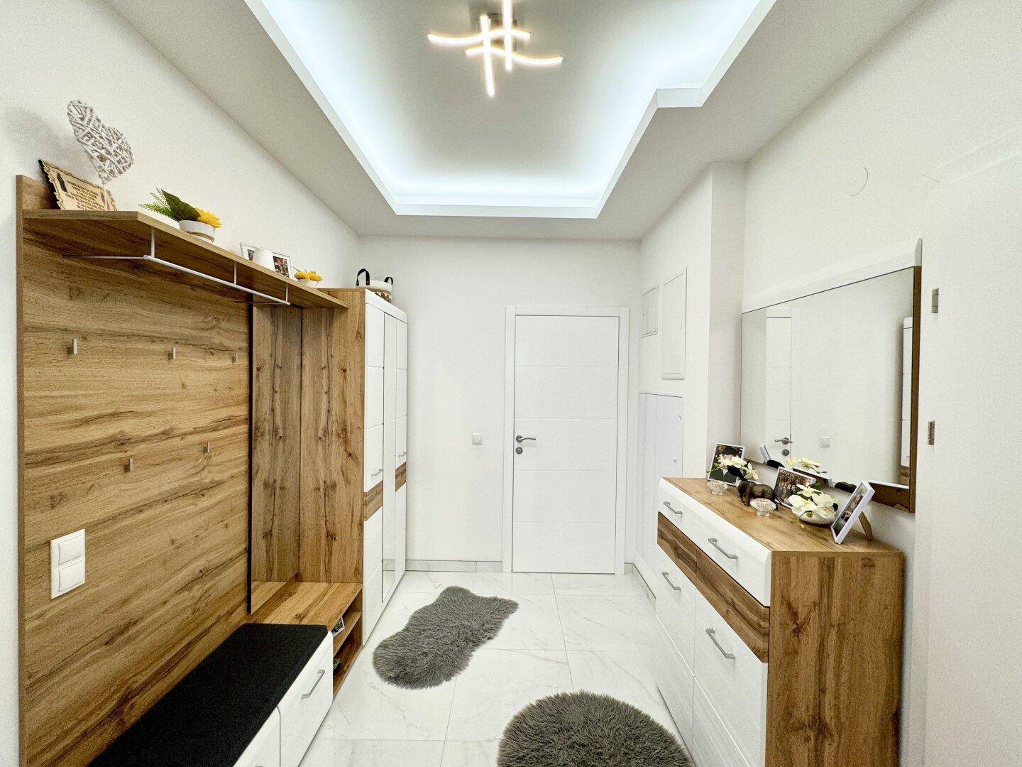 Heller Eingangsbereich mit modernem Garderobensystem, Kommode und eleganten Fliesen, die zum Wohnbereich führen.