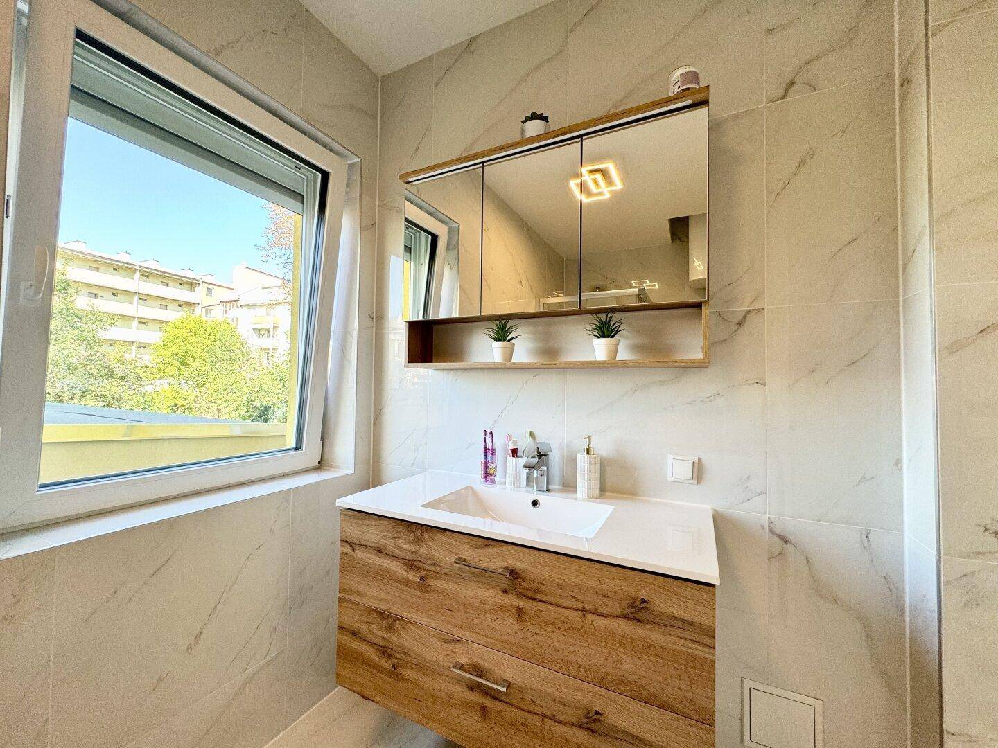 Modernes Badezimmer mit Einzelwaschbecken, Spiegelschrank und großem Fenster für viel Tageslicht.