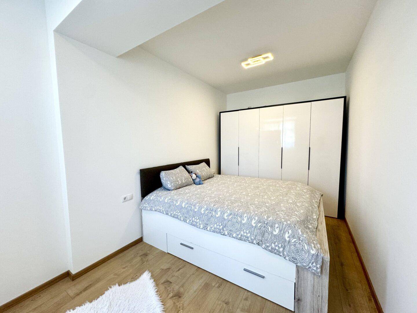 Gemütliches Schlafzimmer mit Doppelbett, integrierten Schubladen und großem weißen Kleiderschrank auf Holzboden.