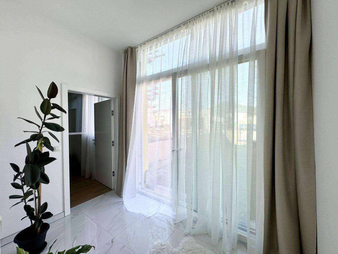 Heller Raum mit großen bodentiefen Fenstern und eleganten Vorhängen, die viel Licht hereinlassen.