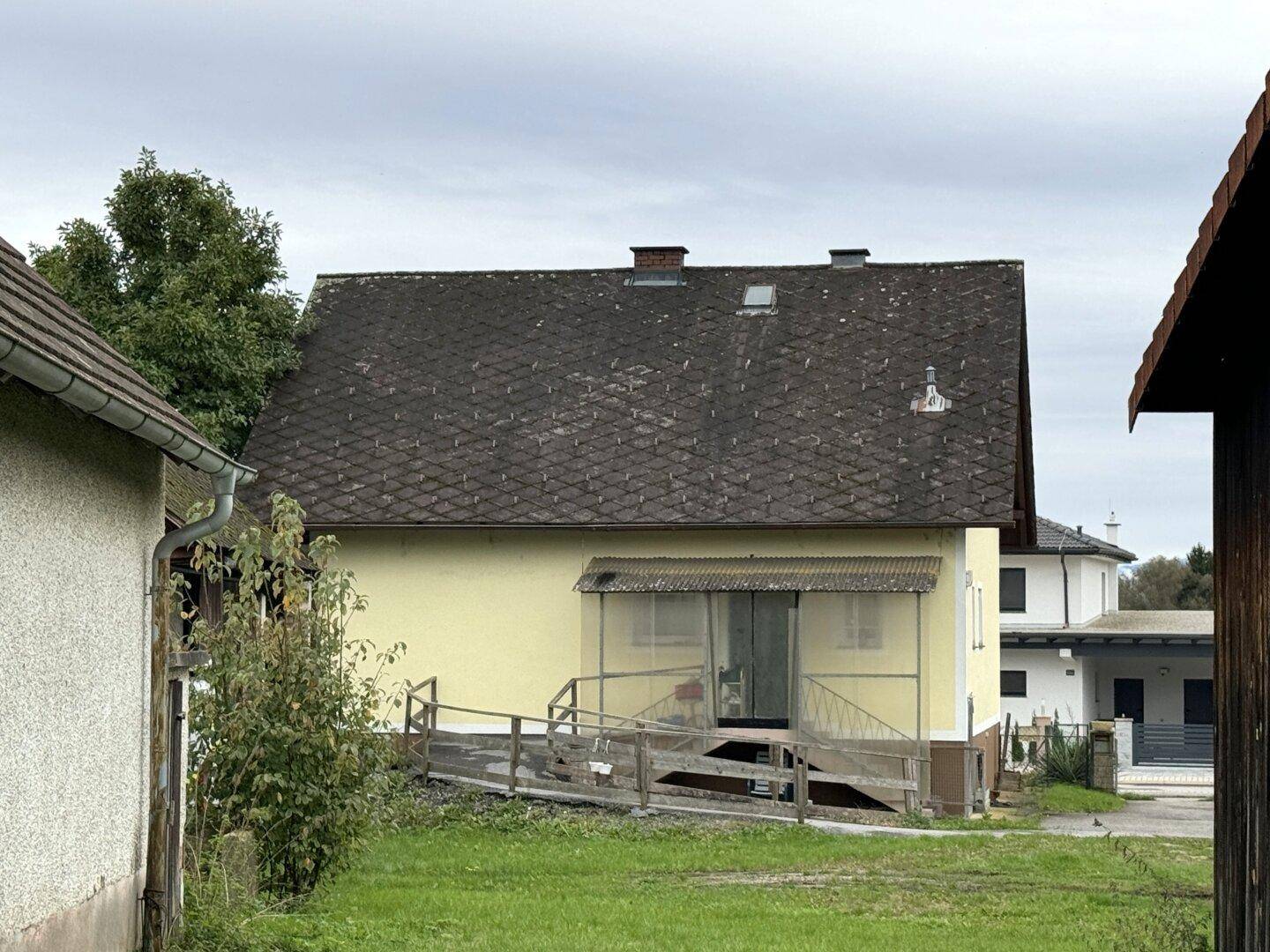 Rückseite des Hauses mit Rampe zum Eingang und einem Satteldach unter bewölktem Himmel.