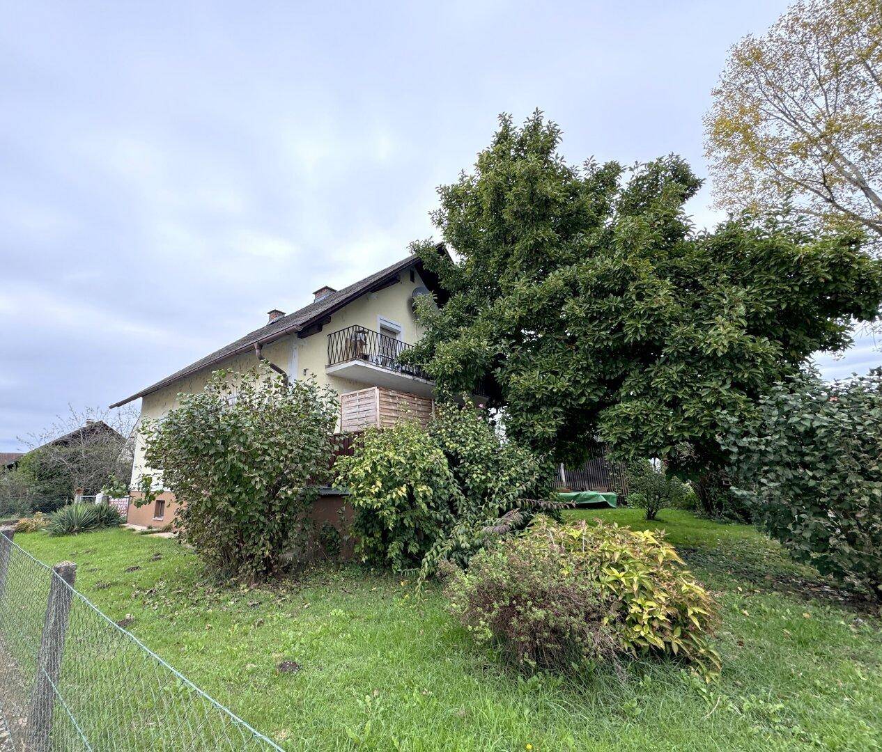Seitenansicht des Hauses mit kleinem Balkon und üppiger Vegetation im Vordergrund.