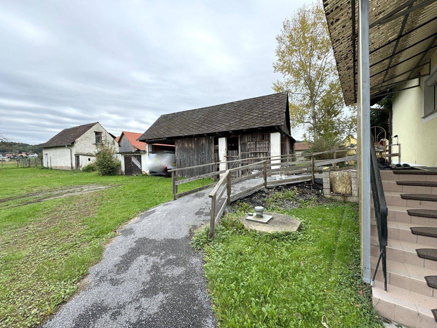 Zufahrt zum Haus mit Rampe und weiteren ländlichen Nebengebäuden im Hintergrund.