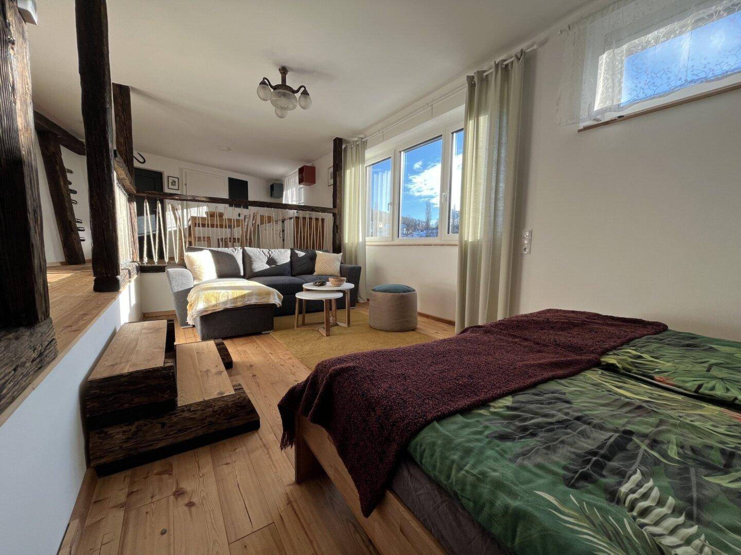 Gemütlicher Schlafbereich mit Holzboden und Blick auf den angrenzenden Wohnbereich mit Sofa.