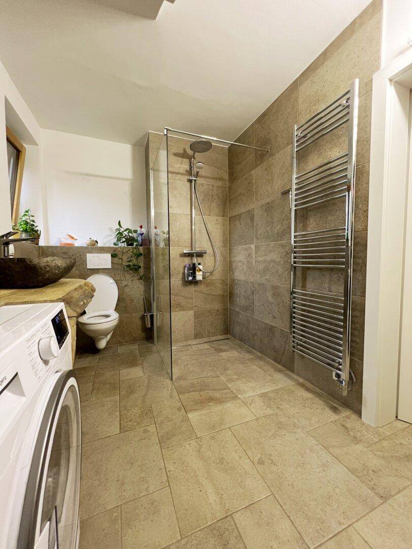 Modernes Badezimmer mit begehbarer Dusche, Wand-WC und beheiztem Handtuchhalter, gefliest.