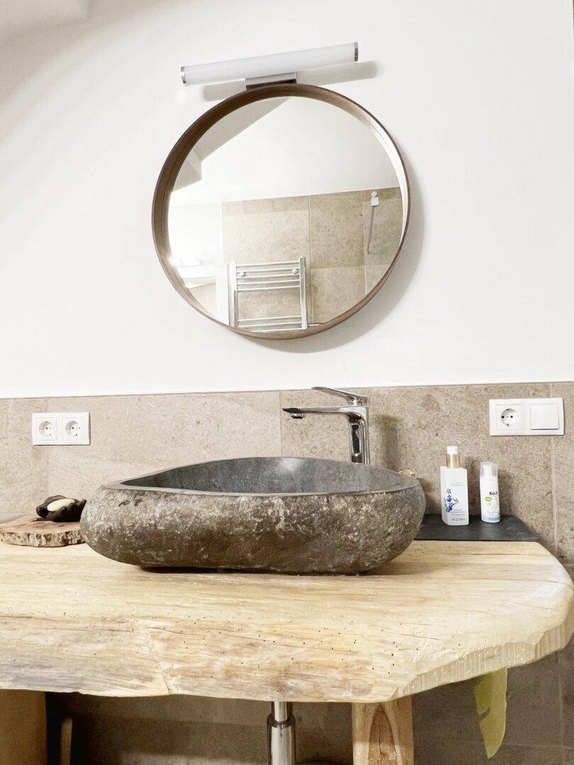 Detailansicht des Badezimmers mit einzigartigem Steinwaschbecken auf einer Holzplatte und rundem Spiegel.