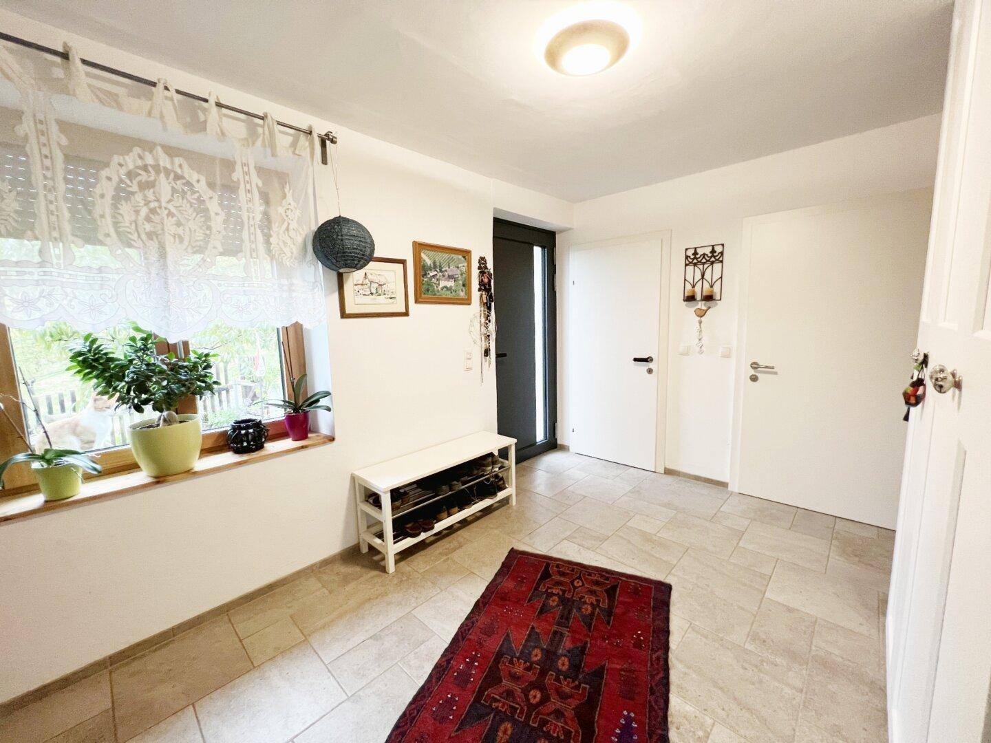 Heller Eingangsbereich mit Fliesenboden, Schuhregal und einem Fenster mit Spitzenvorhängen.