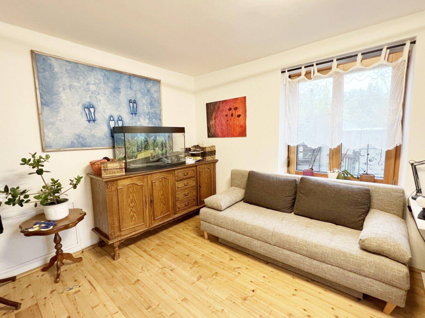 Gemütlicher Wohnraum mit Sofa, Holzschrank, Aquarium und hellem Holzboden.