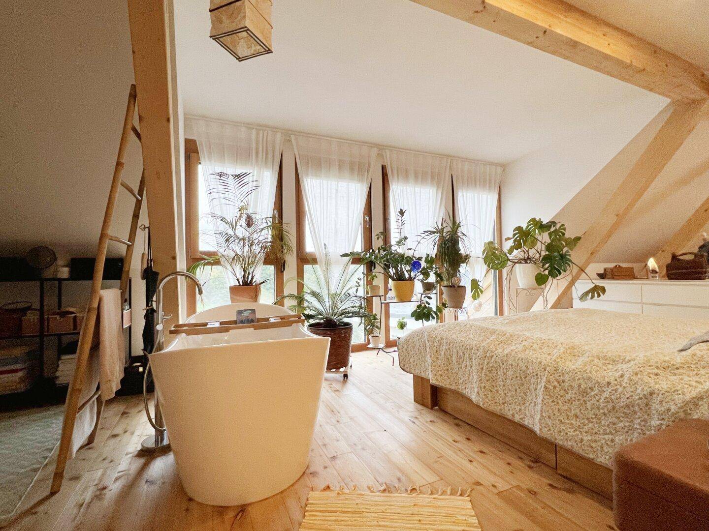 Helles Dachschlafzimmer mit freistehender Badewanne, Holzboden und großen Fenstern.
