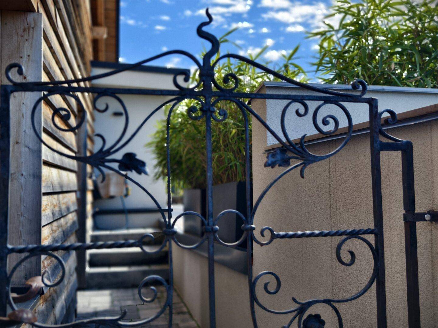 Detailansicht eines kunstvoll geschmiedeten schwarzen Metalltors mit floralen Verzierungen.