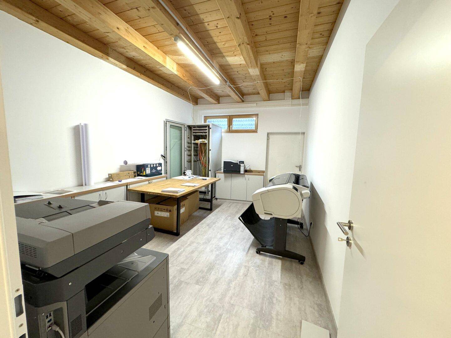 Funktionaler Arbeitsraum mit großen Druckern, Holzbalkendecke und praktischem Fliesenboden.