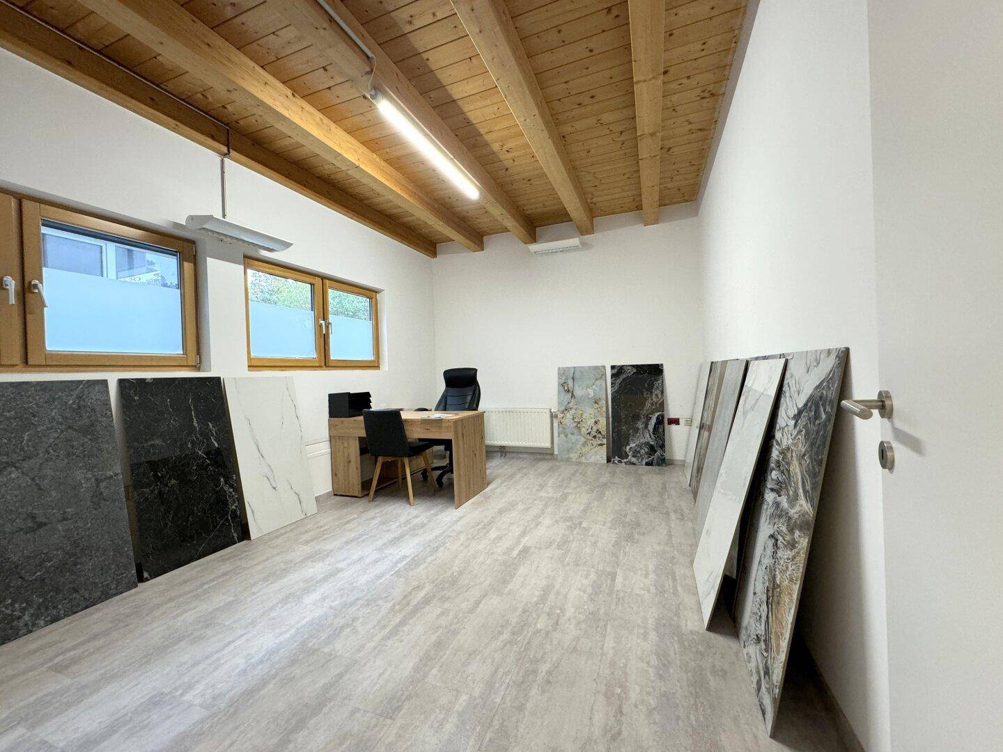 Geräumiges Büro mit Holzbalkendecke, Fliesenboden und verschiedenen Steinplatten als Ausstellungsstücke.