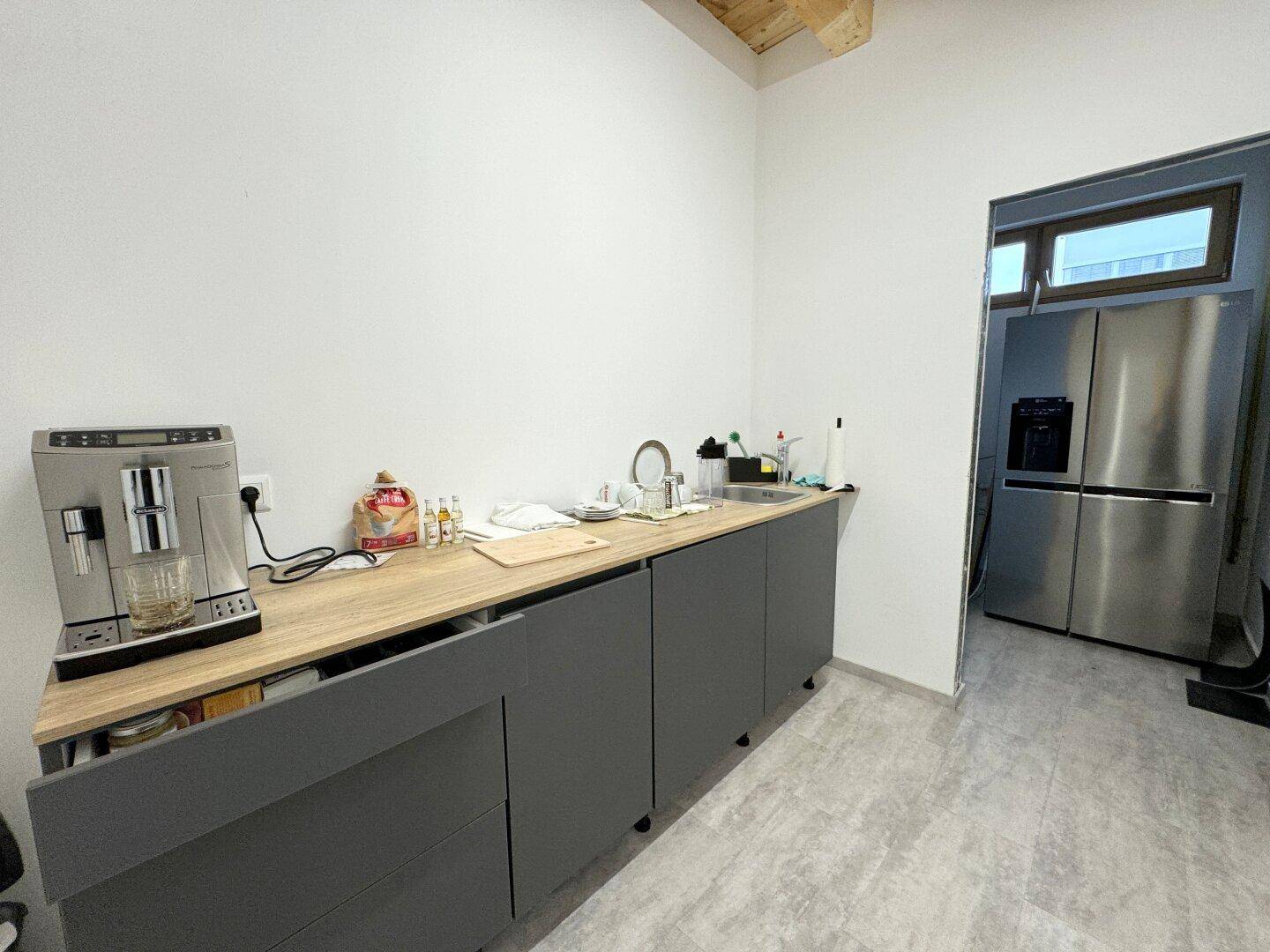 Kleine Küche mit grauen Unterschränken, Holzarbeitsplatte, Spüle und einem großen Kühlschrank.