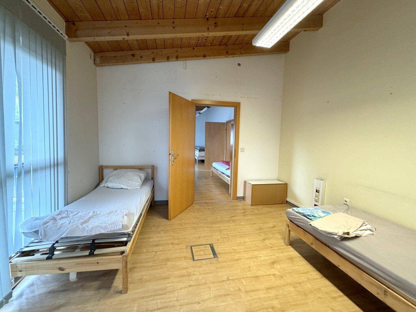 Schlafzimmer mit Holzbalkendecke, Holzfußboden und mehreren Einzelbetten, ideal für Gäste oder Personal.