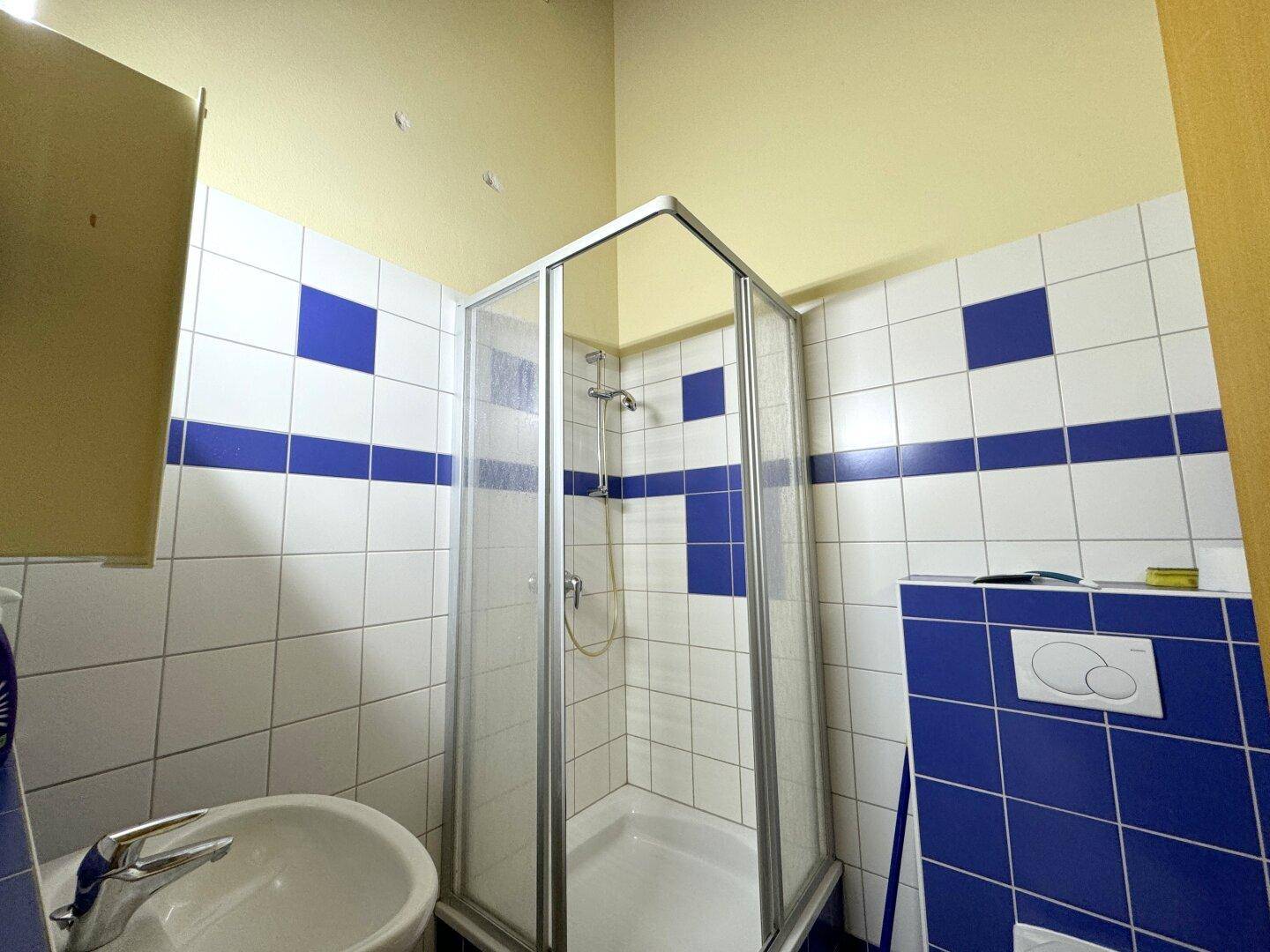 Badezimmer mit blauen und weißen Fliesen, Waschbecken, Toilette und einer Duschkabine.