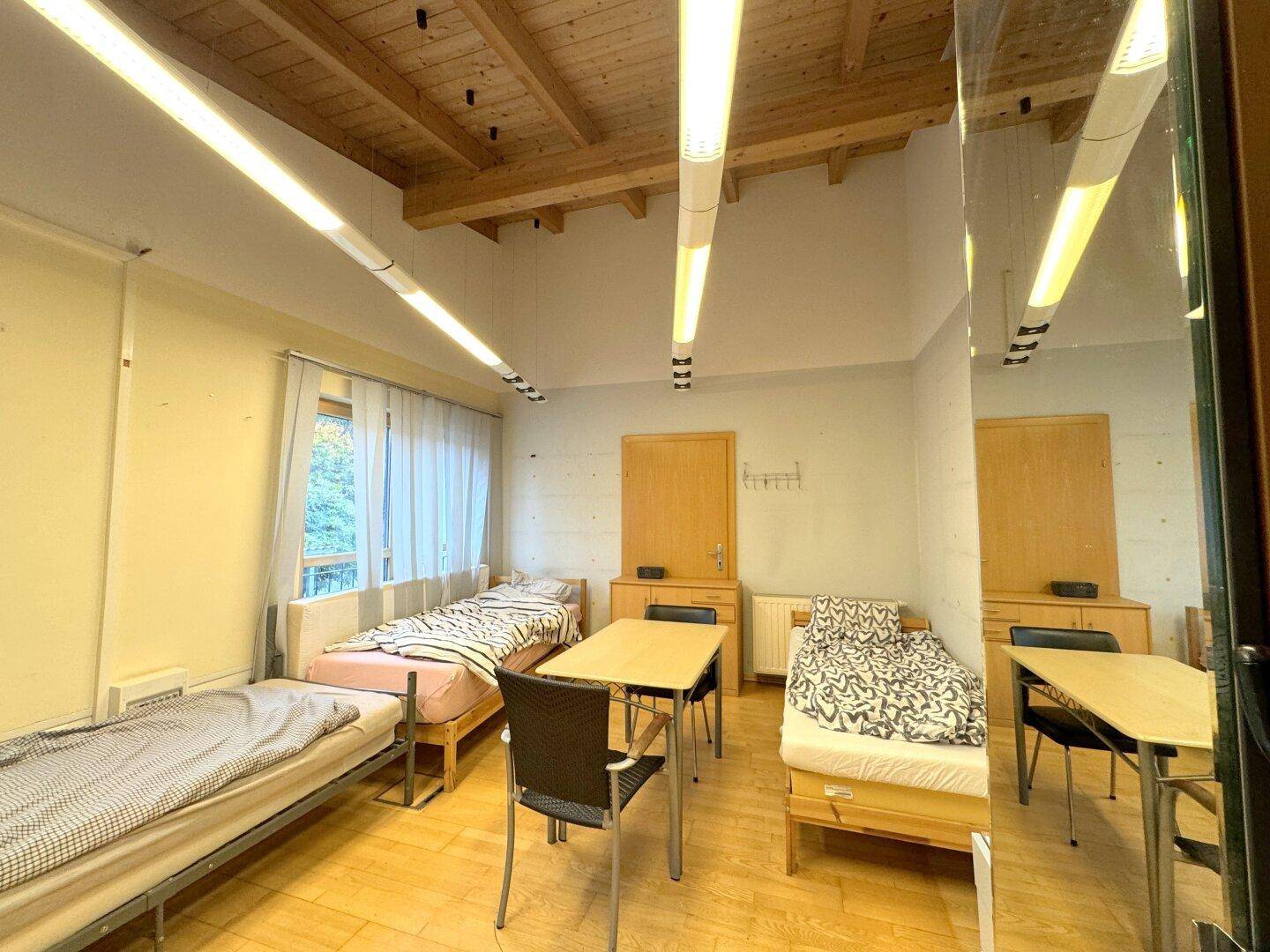 Geräumiges Schlafzimmer mit Holzbalkendecke, Holzfußboden und mehreren Einzelbetten, ideal für Gruppenunterkünfte.