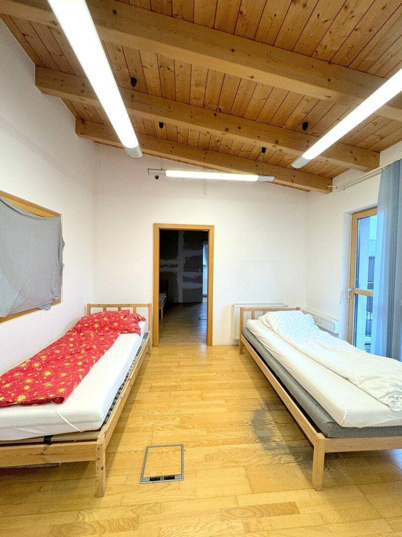 Helles Schlafzimmer mit Holzbalkendecke, Holzfußboden und zwei Einzelbetten.