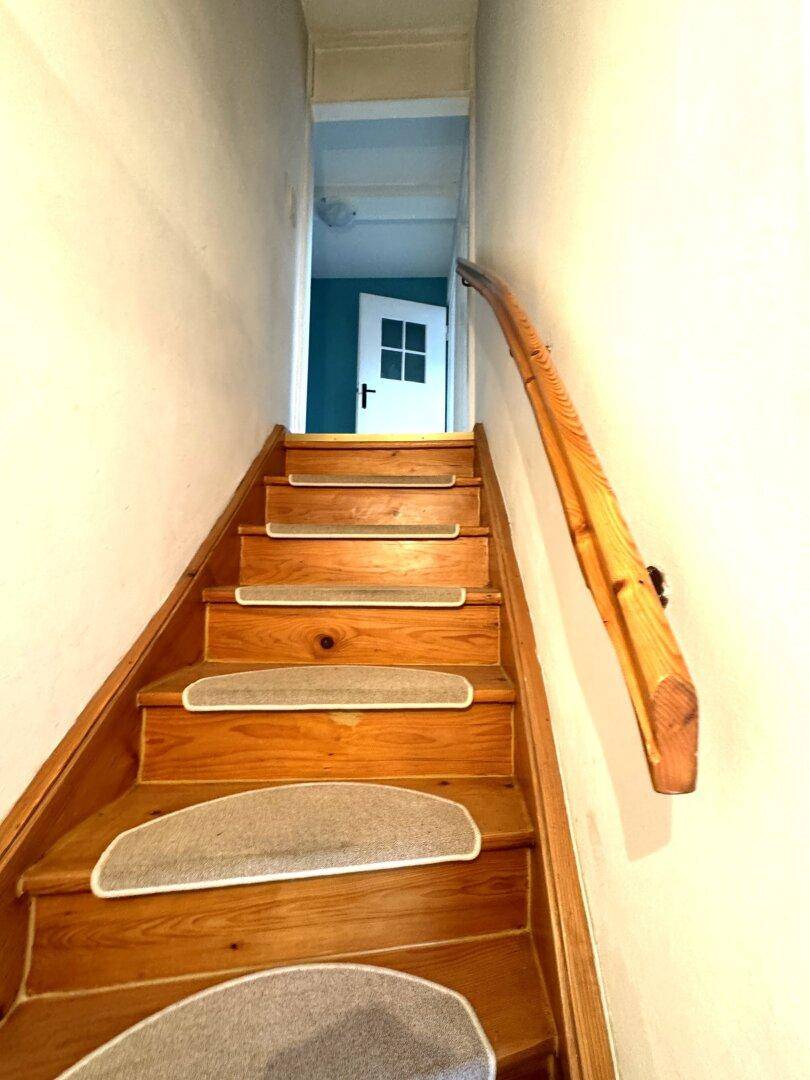 Holztreppe mit Teppichstufen und geschwungenem Handlauf führt in die obere Etage.