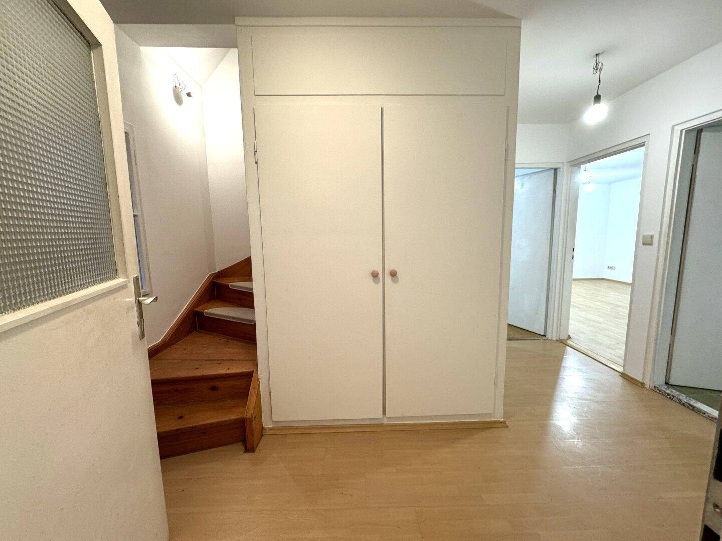 Eingangsbereich mit Holztreppe, Einbauschrank und Zugang zu weiteren Räumen.