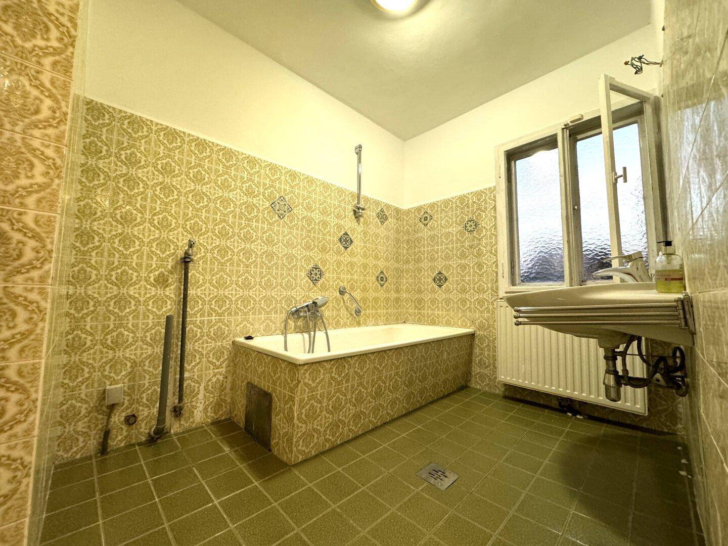 Badezimmer mit Badewanne, Waschbecken und Fenster, ausgestattet mit auffälligen Fliesen.