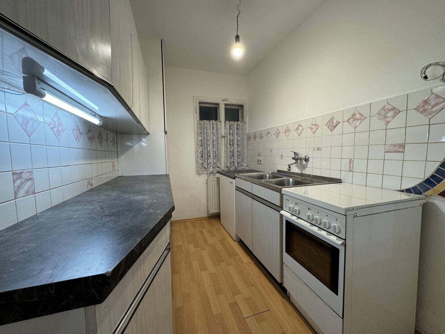 Küche mit weißen Einbauschränken, Spüle, Herd und Fenster, im traditionellen Stil.