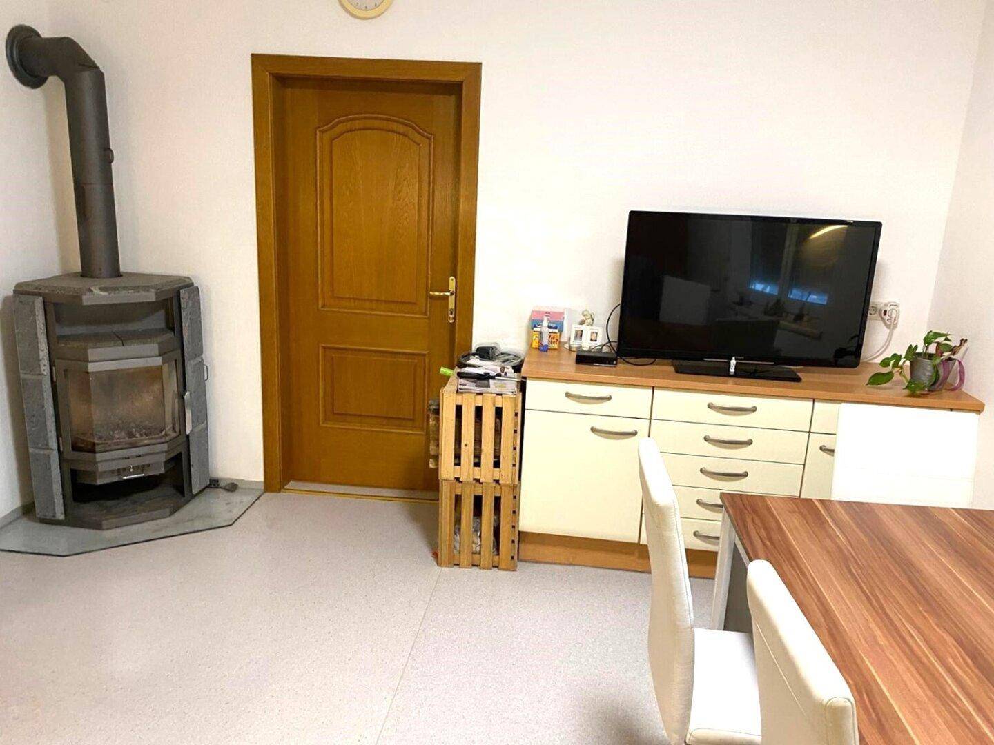 Gemütlicher Wohn-Essbereich mit Kaminofen, Holztür und einem Sideboard mit Fernseher.