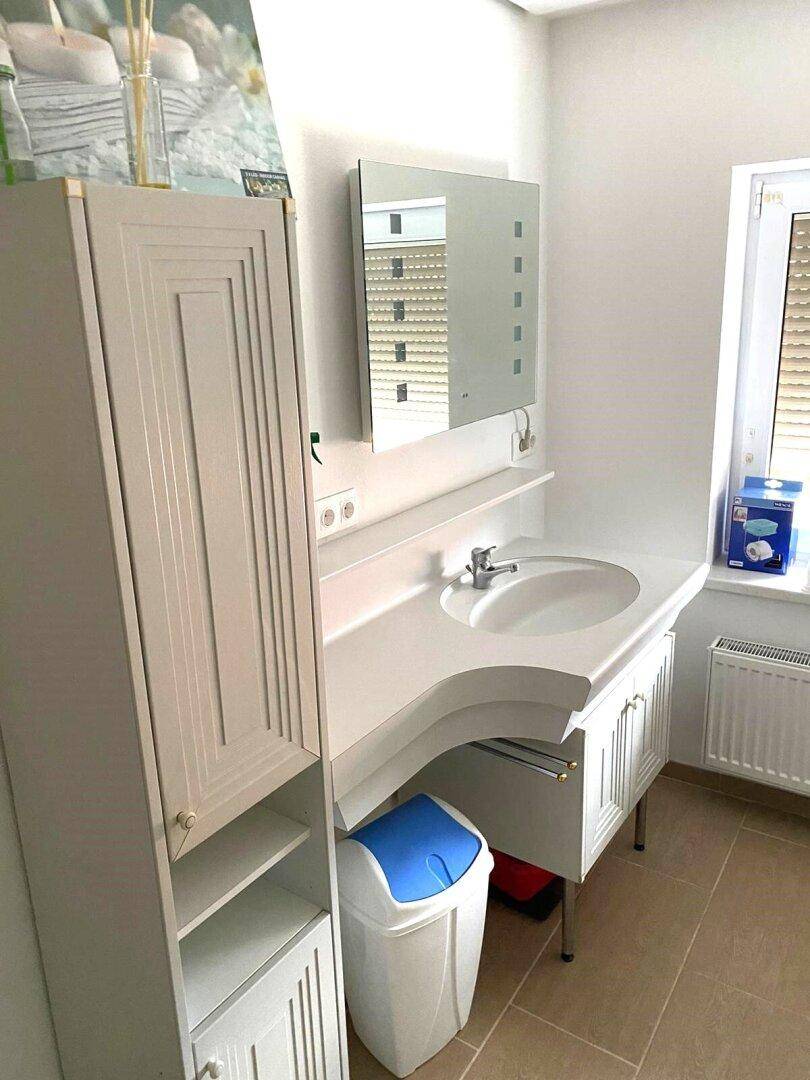 Modernes Badezimmer mit Waschtisch, Spiegelschrank und Fenster mit Heizkörper.