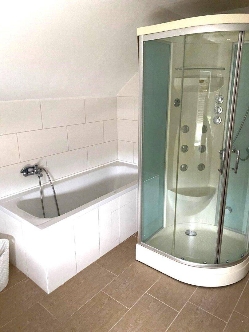 Badezimmer mit Badewanne und Duschkabine, hell gefliest und mit Dachschräge.