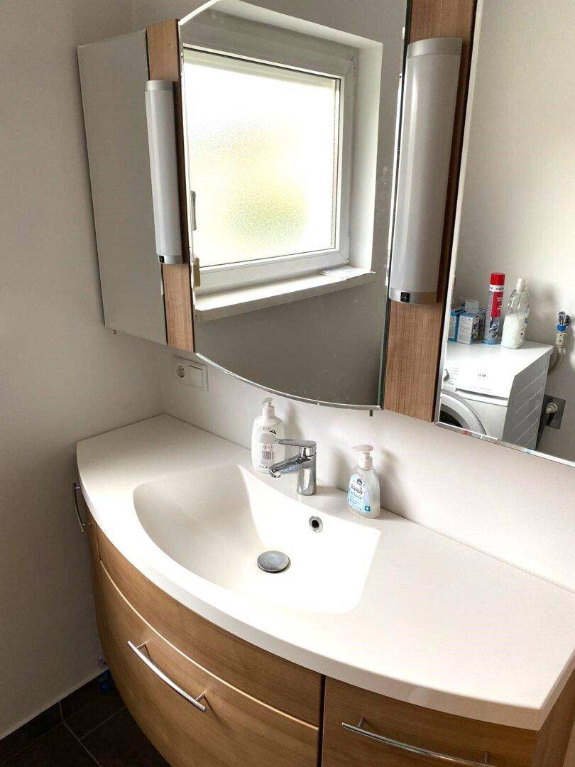 Badezimmer mit modernem Waschtisch, Spiegelschrank und Fenster für natürliches Licht.