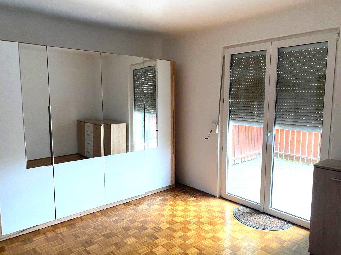 Schlafzimmer mit großem Spiegelschrank, Parkettboden und Zugang zu einem Balkon.