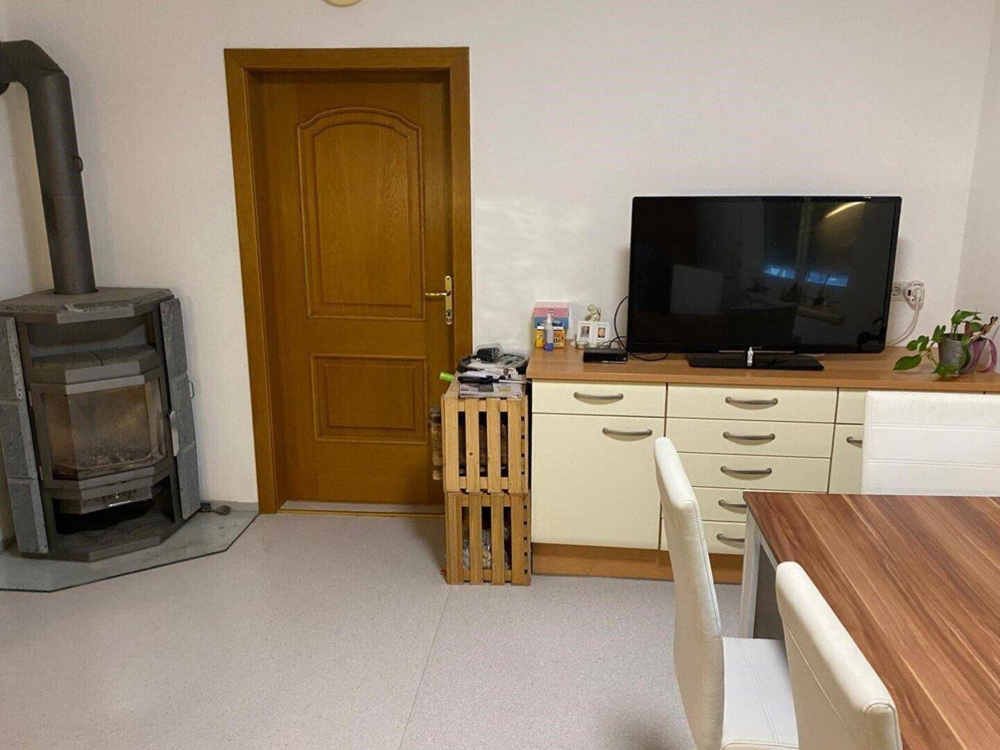 Gemütlicher Wohn-Essbereich mit Kaminofen, Holztür und einem Sideboard mit Fernseher.