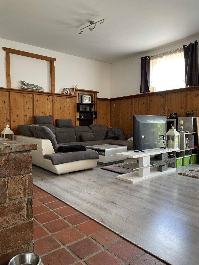 Geräumiges Wohnzimmer mit großer Eckcouch, Holzvertäfelung und modernem Laminatboden.