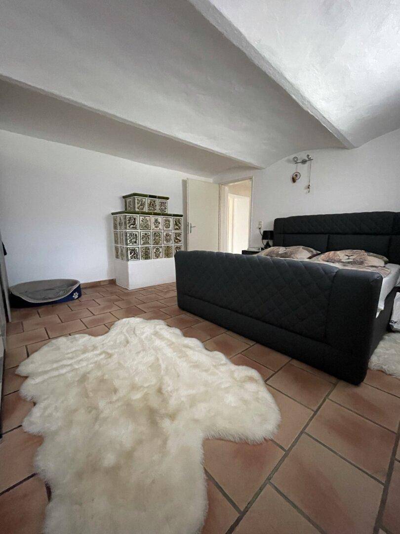 Schlafzimmer mit traditionellem Kachelofen, Terrakottafliesen und gemütlicher Atmosphäre.