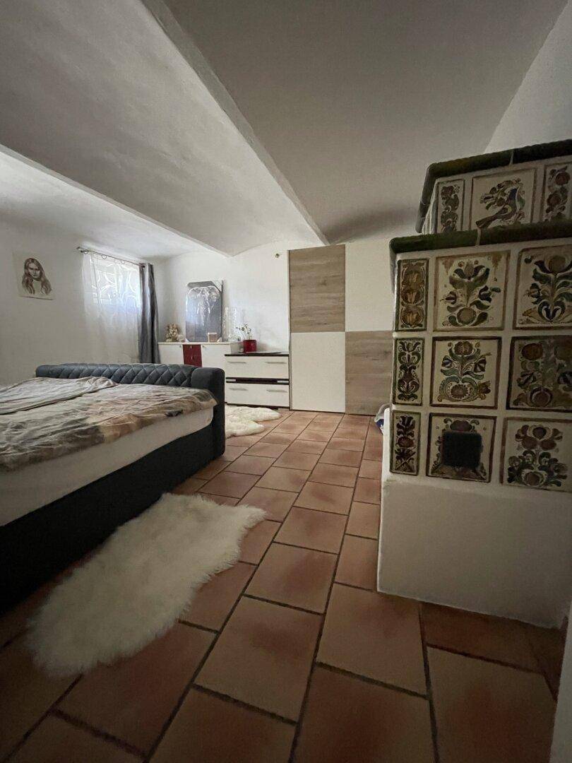 Schlafzimmer mit Doppelbett, Kachelofen und Schränken in Holz- und Weißtönen für Stauraum.