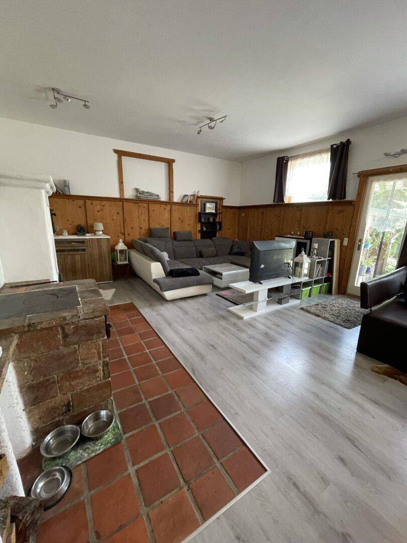 Geräumiges Wohnzimmer mit Kachelofen, großer Eckcouch und Holzvertäfelung an den Wänden.