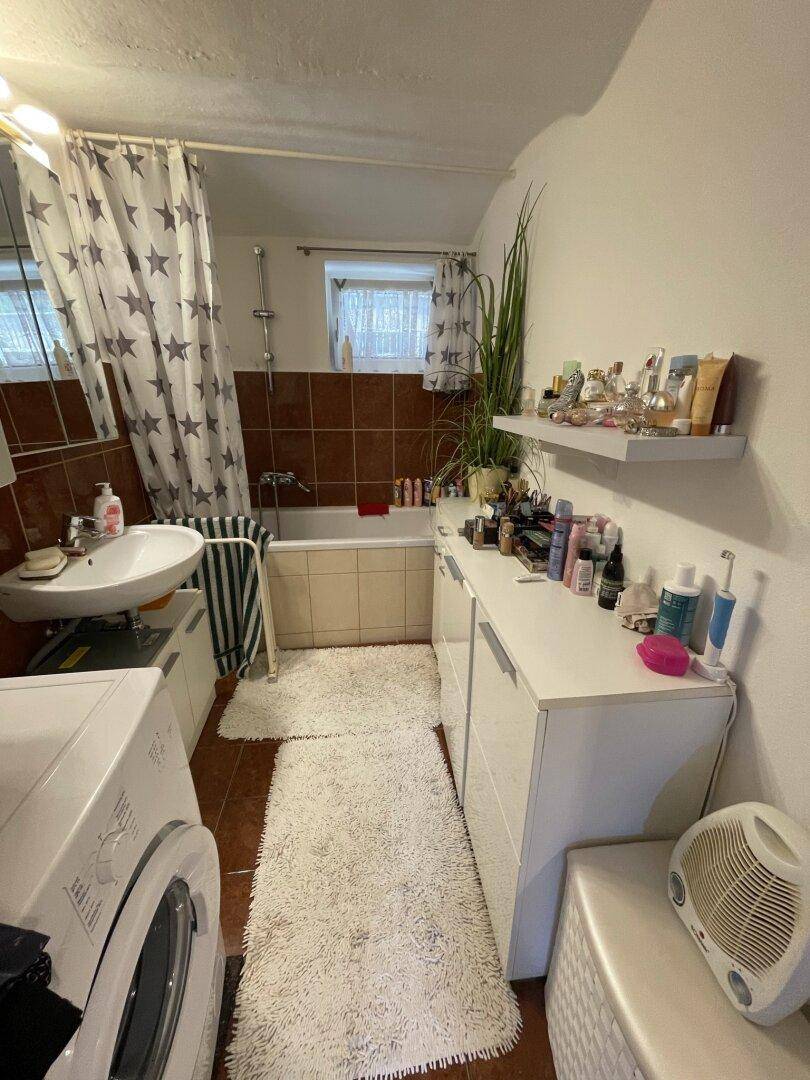 Badezimmer mit Badewanne, Waschbecken, Waschmaschine und Fenster für Tageslicht.