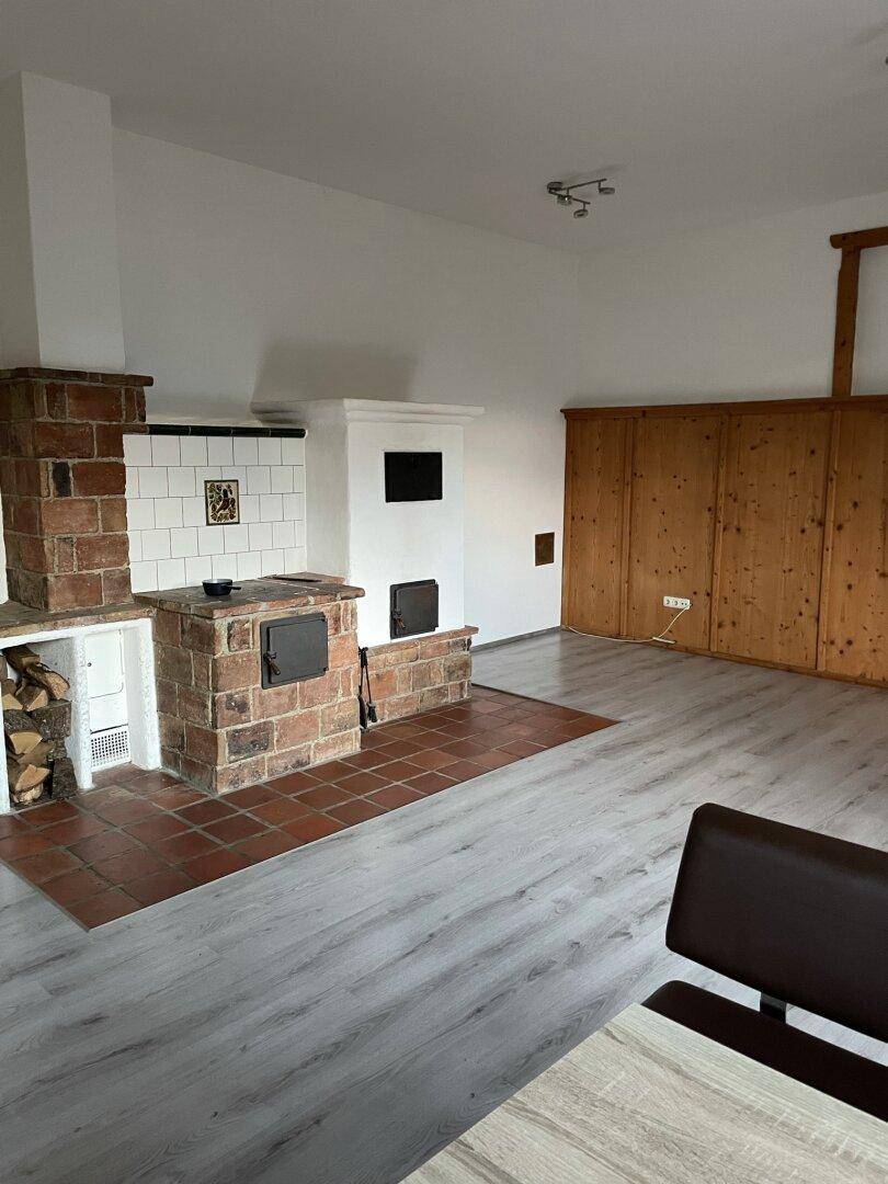 Geräumiges Wohnzimmer mit traditionellem Kachelofen, Holzvertäfelung und modernem Laminatboden.