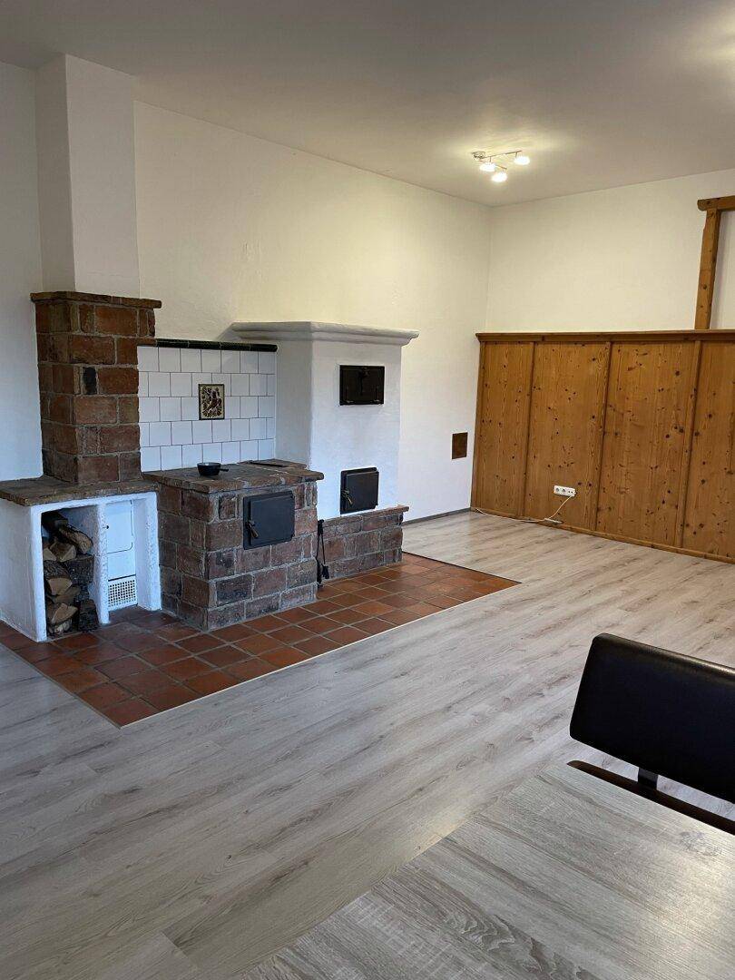 Geräumiges Wohnzimmer mit traditionellem Kachelofen, Holzvertäfelung und modernem Laminatboden.