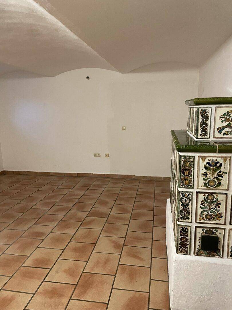 Raum mit gewölbter Decke, Terrakottafliesen und einem verzierten Kachelofen in traditionellem Stil.
