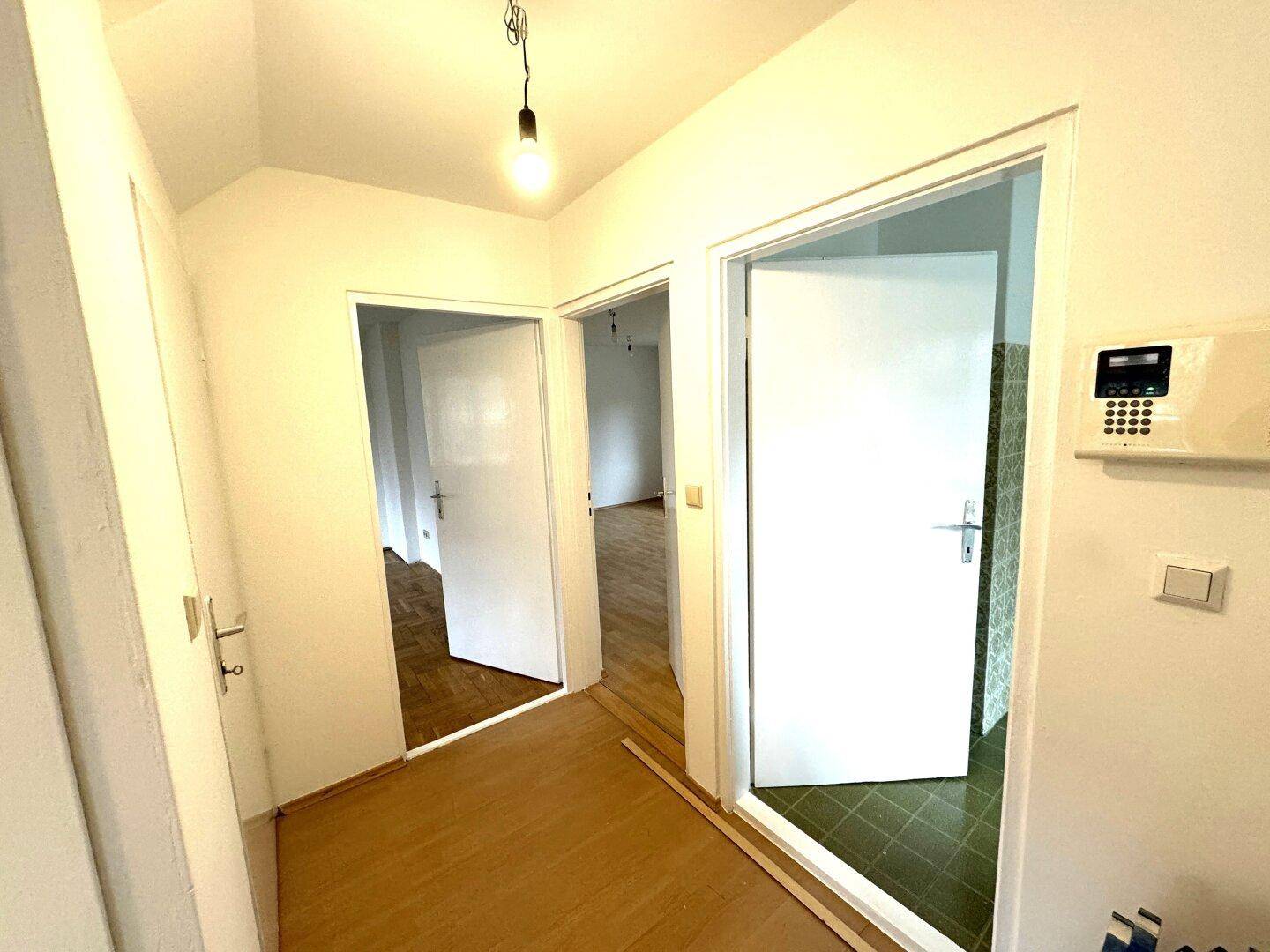 Heller Flur mit mehreren Türen, Laminatboden und einer Sicherheitstafel an der Wand.