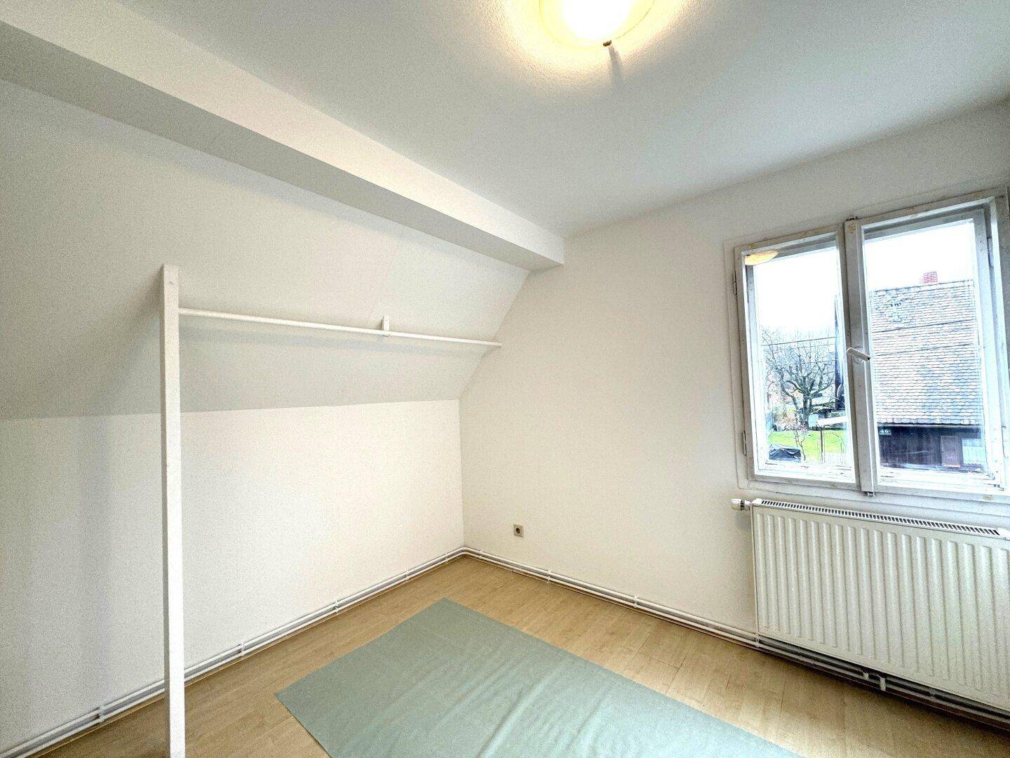 Helles Schlafzimmer mit Laminatboden, Dachschräge und Fenster mit Blick nach draußen.