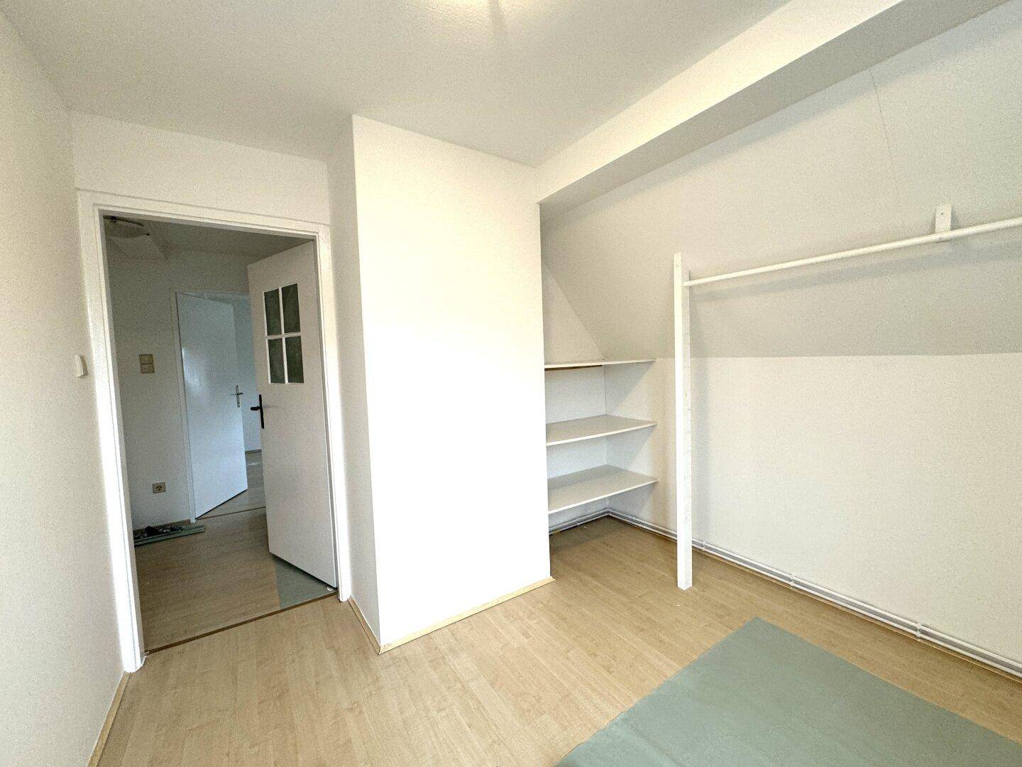 Schlafzimmer mit Laminatboden, praktischen Regalen und Zugang zu einem weiteren Raum.