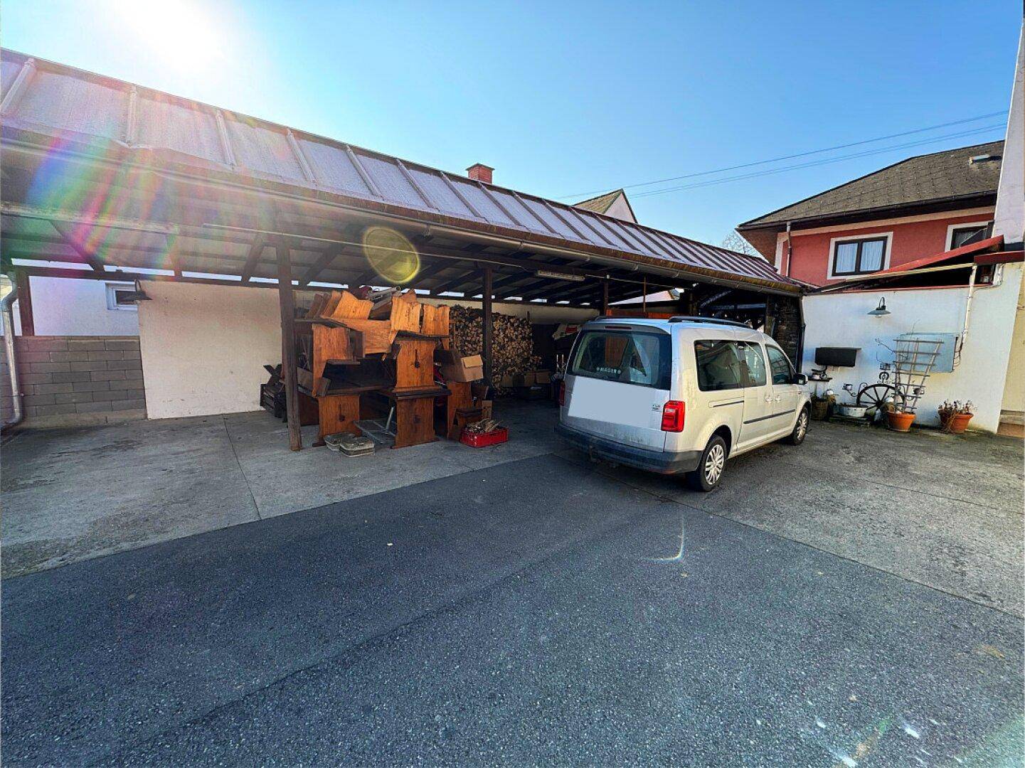 Überdachter Bereich mit Holzstapeln und einem geparkten Fahrzeug.