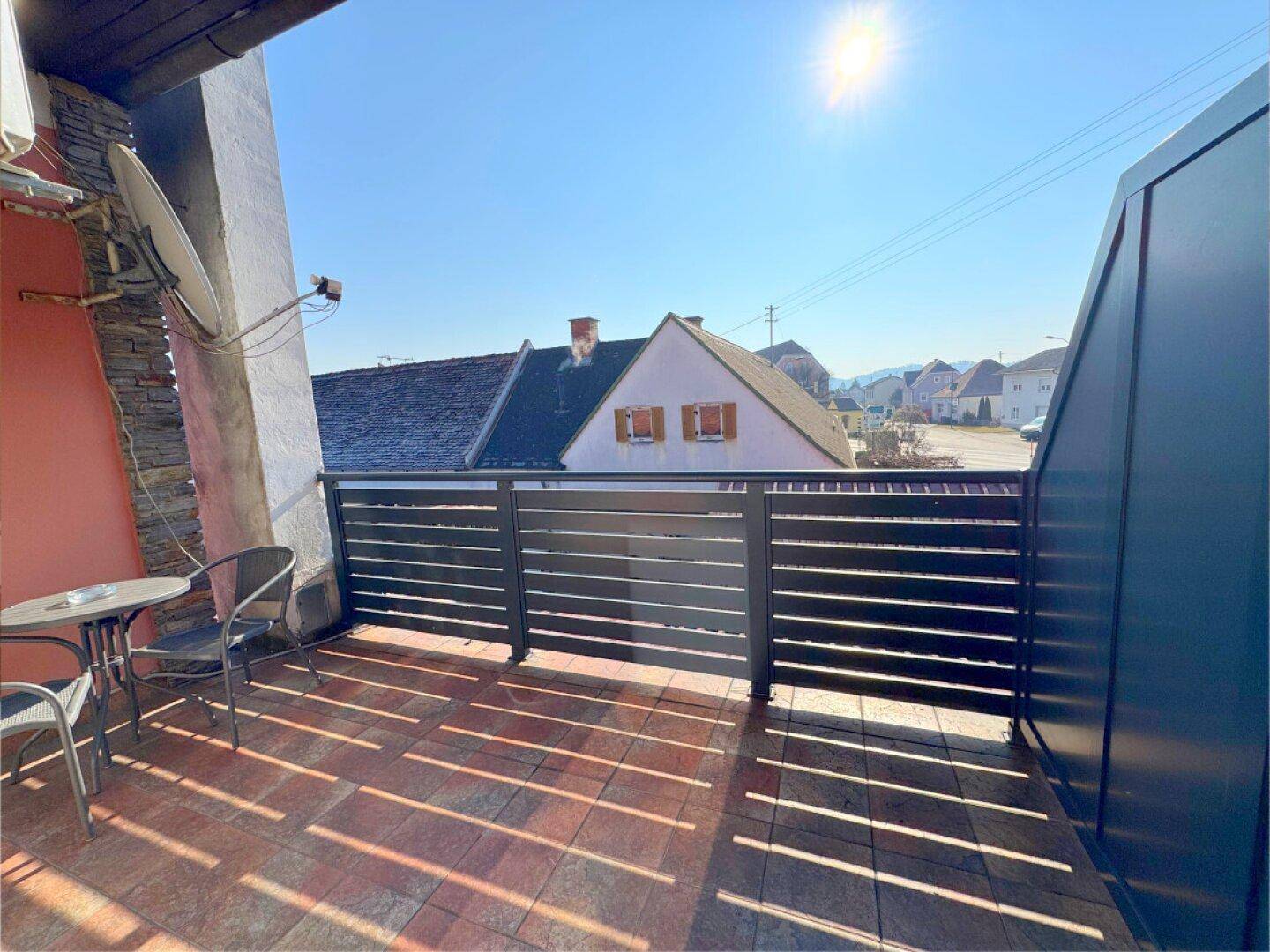 Sonniger Balkon mit Fliesenboden, Metallgeländer und Blick auf die Umgebung.
