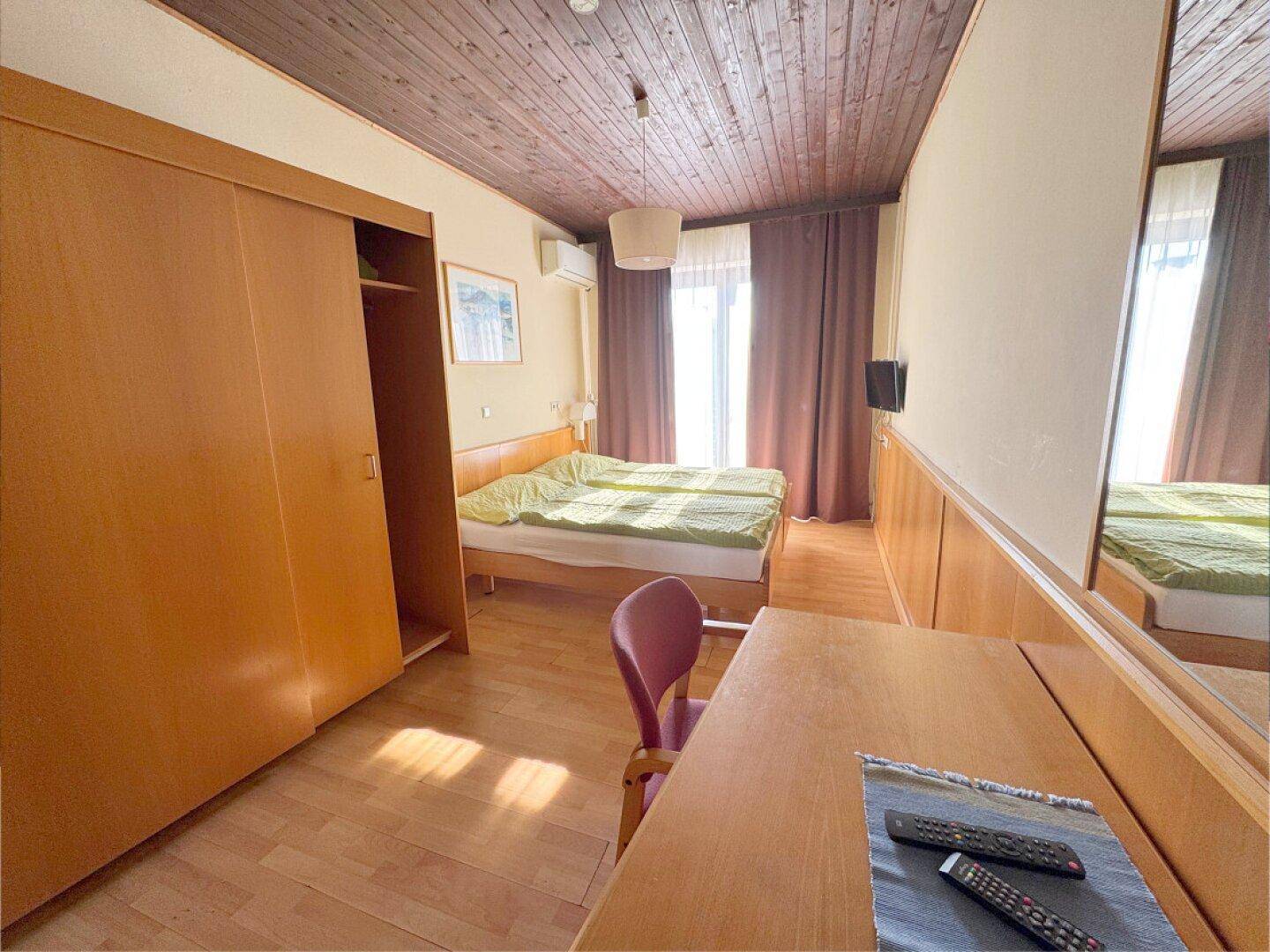 Gemütliches Schlafzimmer mit Holzdecke, Doppelbett, Schiebetürenschrank und Klimaanlage.