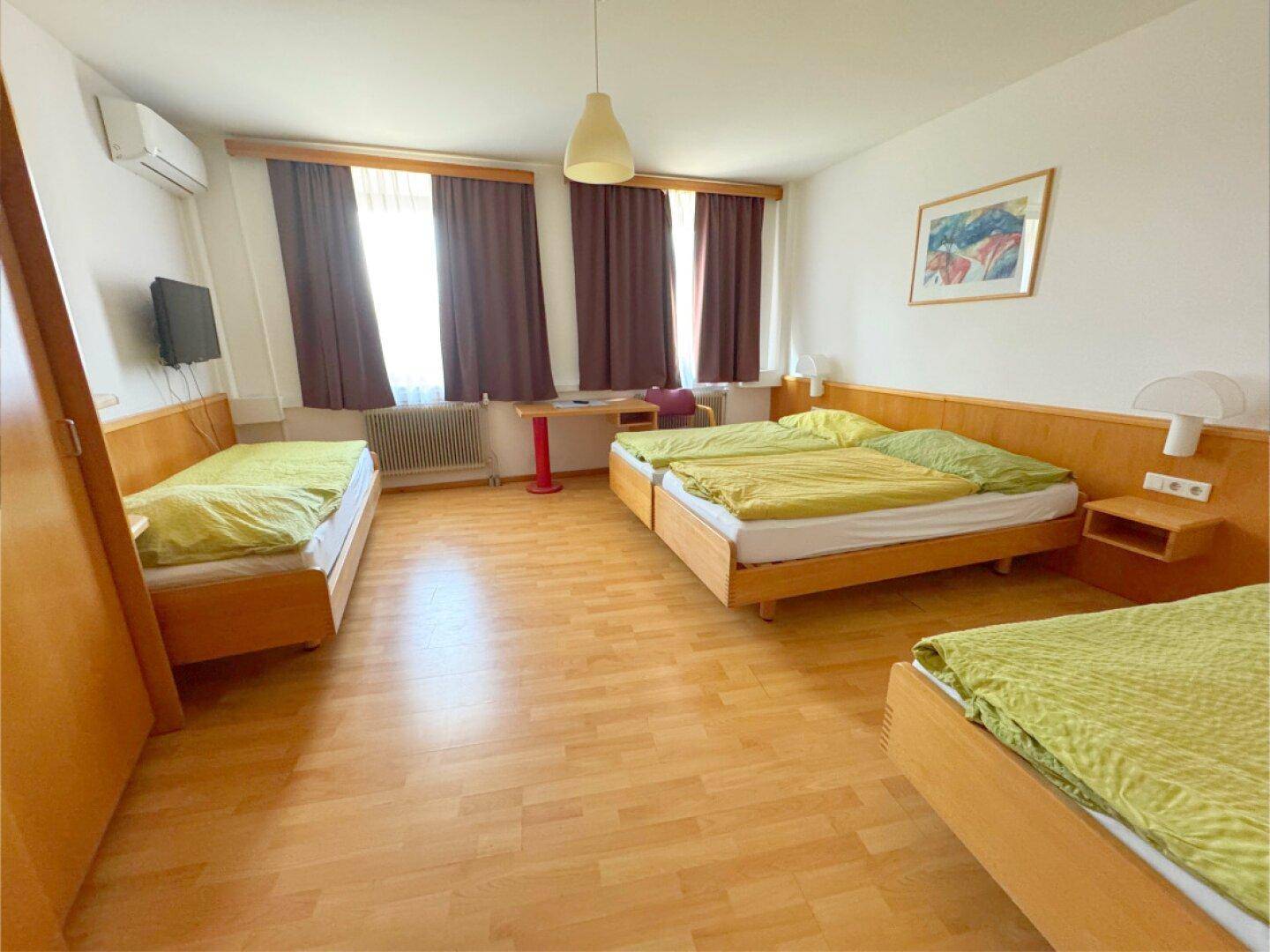 Helles Schlafzimmer mit mehreren Betten, Laminatboden und Klimaanlage.