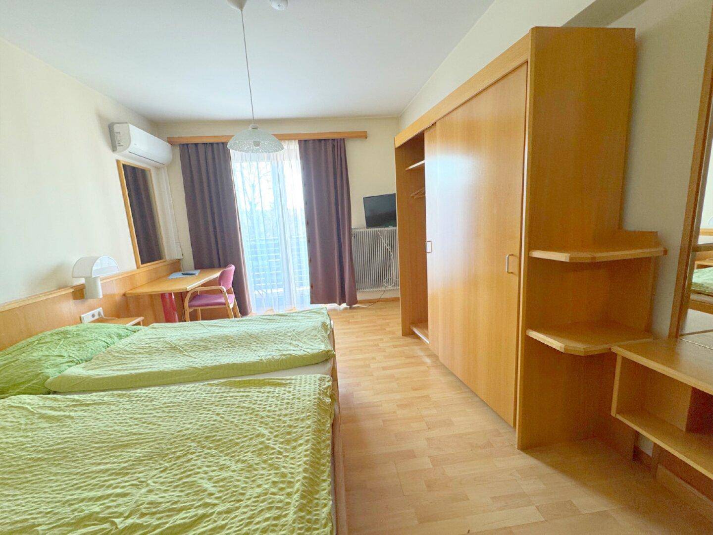 Helles Schlafzimmer mit Doppelbett, Schiebetürenschrank, Klimaanlage und Balkonzugang.