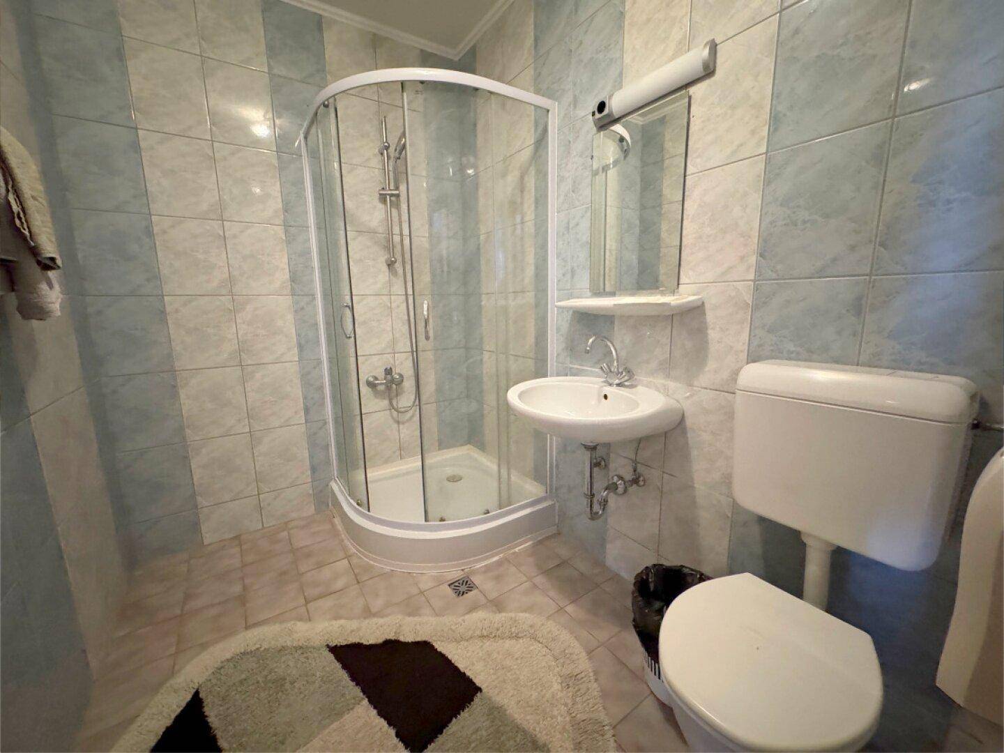 Badezimmer mit Duschkabine, WC und Waschbecken, gefliest in hellblauen und weißen Streifen.